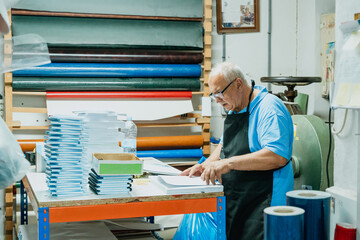 Attentive elderly male worker checking papers in printing studio