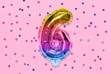 Rainbow foil balloon number, digit six on a pink background with sequins. Birthday greeting card with inscription 6. Top view. Numerical digit. Celebration event, template.