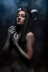 Halloween holiday. A girl with horns and black eyes in the smoke. Demon, smoke, fear, fantasy