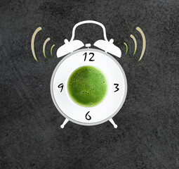 Tasty matcha tea in a white cup and alarm clock on grey textured background. Waking up with matcha...