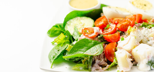 Healthy salad, potato salad with hard boiled egg, shredded ham, cucumber, tomatoes, lettuce and spinach with a honey and mustard dressing pot