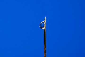 a drop of solution at the end of a medical syringe on a blue background macro. Medicine injection medicine health