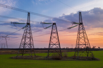 silhouette of high voltage power lines against a colorful sky at sunrise.