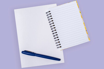 White sheet of papper and an open notebook with a dark blue marker on a violet background