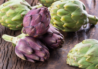 Obraz premium Green and purple artichoke flower edible buds on wooden background.