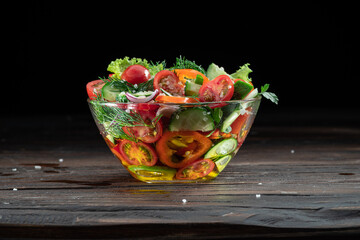Vegetable salad with leafy greens in the glass oil is on the wooden table.