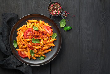 Penne pasta with tomato and meat bolognese sauce and fresh basil on a black background.