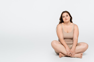 Obraz premium Brunette woman with overweight sitting with crossed legs on grey background.