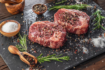 Raw Ribeye steaks with salt and herbs on grey board. Top view.