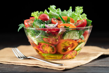 Vegetable salad with leafy greens in the glass oil is on the wooden table.