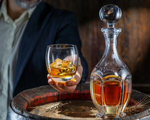 Whisky tasting. Man sits in front of a barrel with a decanter and a glass of whiskey.