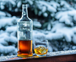 Bottle of whisky and glass of whisky on wooden board. Snowy winter background.