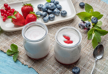 Two glass containers with plain yoghurt and berries on the table. Light summer mood.