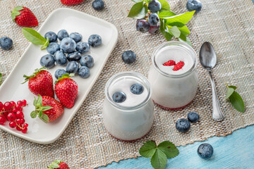 Obraz na płótnie Canvas Two glass containers with plain yoghurt and berries on the table. Light summer mood.