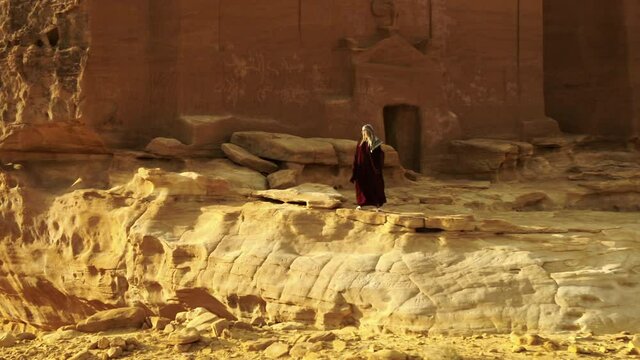 Aerial Circling A Woman Dressed In Red As She Stands At The Entrance Of A Large Ancient Desert Tomb - Arabian Desert, Saudi Arabia
