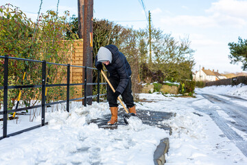 A young man clearing the footpath of snow and ice to make it safe to walk on during a heavy snowfall. Winter safety, clearing snow and ice concept