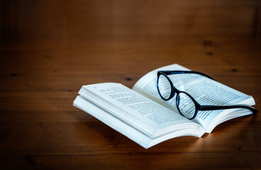 Ein aufgeschlagenes Buch und eine Brille auf einem Holztisch
