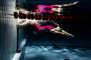 Underwater shooting. One female swimmer training at pool, indoors. Underwater view of swimming...