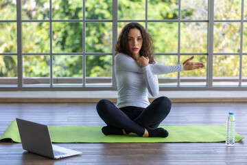 young athletic woman doing stretching exercises for arm muscles watching online tutorials on laptop