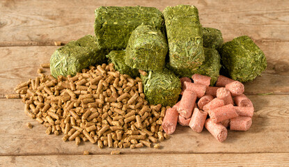 Pelleted horse feed on left, green alfalfa-timothy cubes in the middle, and pink peppermint treats on the right; on rustic wooden table - 467391008