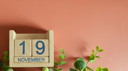 November 19, Date design with calendar cube and leaf on orange background.