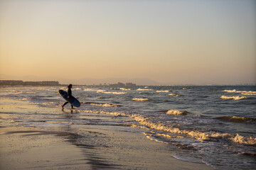 Silhouette of a surfer with long hair walking towards the sea holding a surfboard