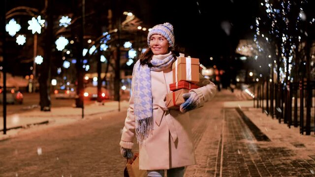 holidays and people concept - happy woman with christmas gifts and shopping bags walking in winter city over snow