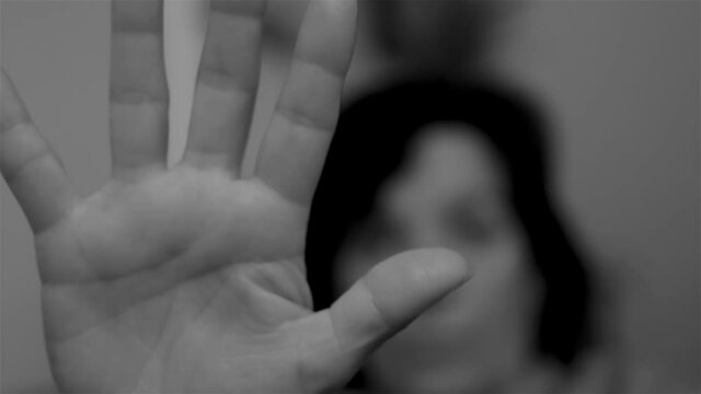 Black and white video of a woman extends her open hand as a sign to stop sexist violence