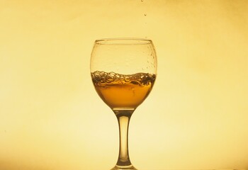 A drink (juice, wine, cocktail) is poured into a transparent glass. Photo on a yellow background.