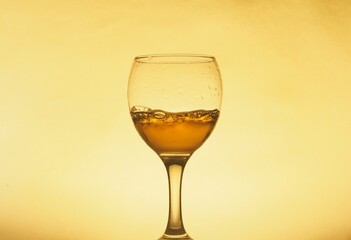 A drink (juice, wine, cocktail) is poured into a transparent glass. Photo on a yellow background.