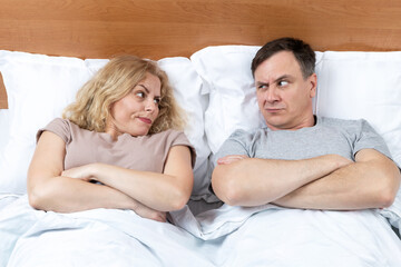 Two, a man and a woman lie on the bed and look at each other with displeasure. Relationship concept 