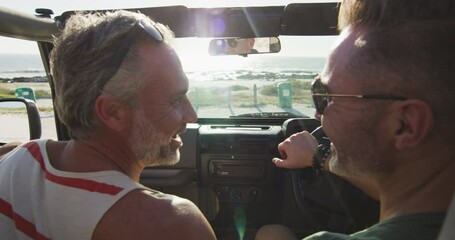 Happy caucasian gay male couple driving car and talking on sunny day at the beach