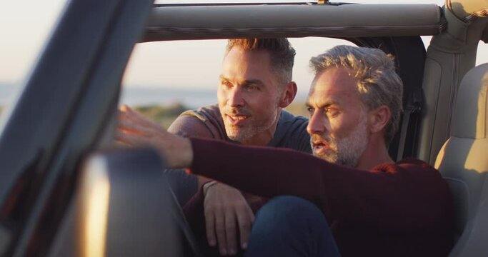 Happy caucasian gay male couple sitting in car admiring the view and talking at the beach