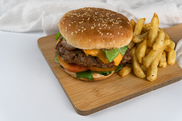 Tasty gourmet hamburger of beef, bacon, cheese and vegetables with fries on a wooden board. Aesthetic hamburger concept on light colors