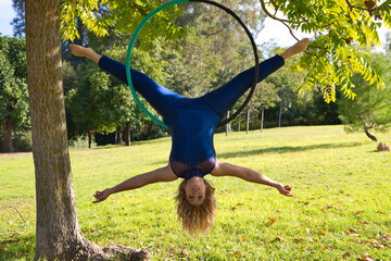 Blonde woman and young gymnast acrobat athlete performing aerial exercise on air ring outdoors in park. Lithe woman in blue costume performs poses of circus performers dancing with hips