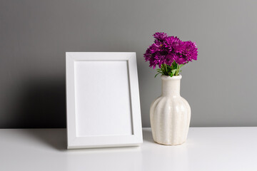 Portrait white frame mockup for artwork, photo and print presentation. Grey walll interior with fresh chrysanthemum flowers in vase.