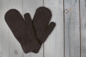 Warm woolen mittens of dark color on a light wooden background. Winter clothing and accessory. Flat lay, top view.