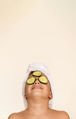 Child relaxes on a spa day. Child with towel on head and cucumber on face. Children's concept, skin care and relaxation.