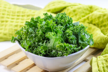 Fresh green curly cabbage or kale salad leaves cut in the bowl on light background on the table in...