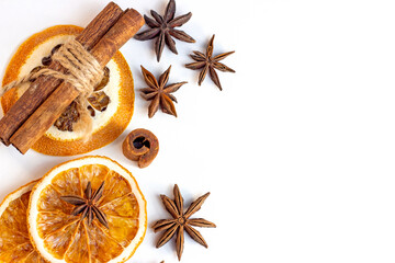 Top view flat lay of Christmas spices for traditional beverages: cinnamon sticks, anise stars, dry orange slices as a frame for Xmas seasonal decorations on white background with copy space.
