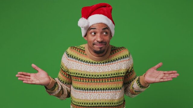 Confused shy young african american Santa man 20s wears shirt Christmas hat look around spread hands say oops ouch oh omg i am so sorry isolated on plain olive green khaki background studio portrait
