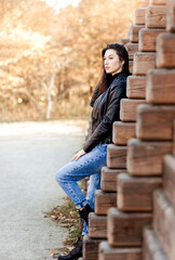 A young brunette woman in a black leather jacket in the park in the fall. Walking to the city street.