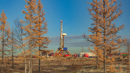 Landscape of an oil and gas field in the northern forest-tundra of Siberia. The main object is a drilling rig that blends into the picturesque autumn landscape of taiga trees