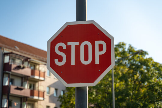 A stop sign in front of a tree and a residential building on a sunny day. Traffic symbols in a German city to make car drivers cautious and careful to prevent accidents.