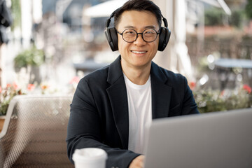 Asian businessman in earphones working on laptop in cafe. Concept of remote and freelance work....