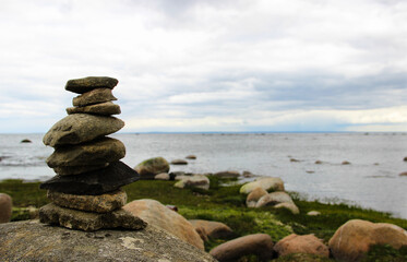Pyramid made by stones. Stone tower and sea in the background. Stone pile was made by tourist in coastline. Rocks on the coast of the Sea. Beautiful seascape. Concept of balance, harmony and vacation.