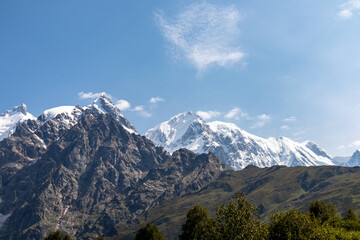 Fototapeta premium A panoramic view on the snow-capped peaks of Tetnuldi, Gistola, Lakutsia and Jangi-Tau(Dzhangi-Tau) in the Greater Caucasus Mountain Range in Georgia, Svaneti Region. Sharp peaks, wanderlust.