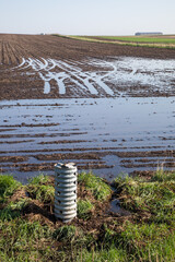 Agricultural drainage tile at the field edge of a wet area. Wheel tracks in the field show potential compaction areas as soil wetness can exacerbate compation.