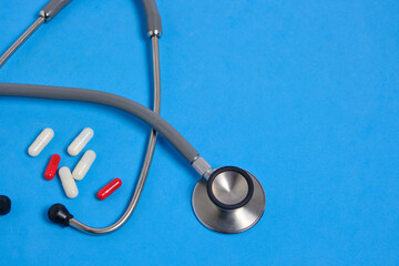 Stethoscope and bunch pills on blue background.