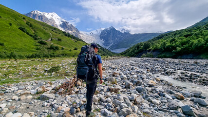 A man enjoying the panoramic view on the snow-capped peaks of Tetnuldi, Gistola and Lakutsia in the Greater Caucasus Mountain Range in Georgia, Svaneti Region. Wanderlust, backpacking.